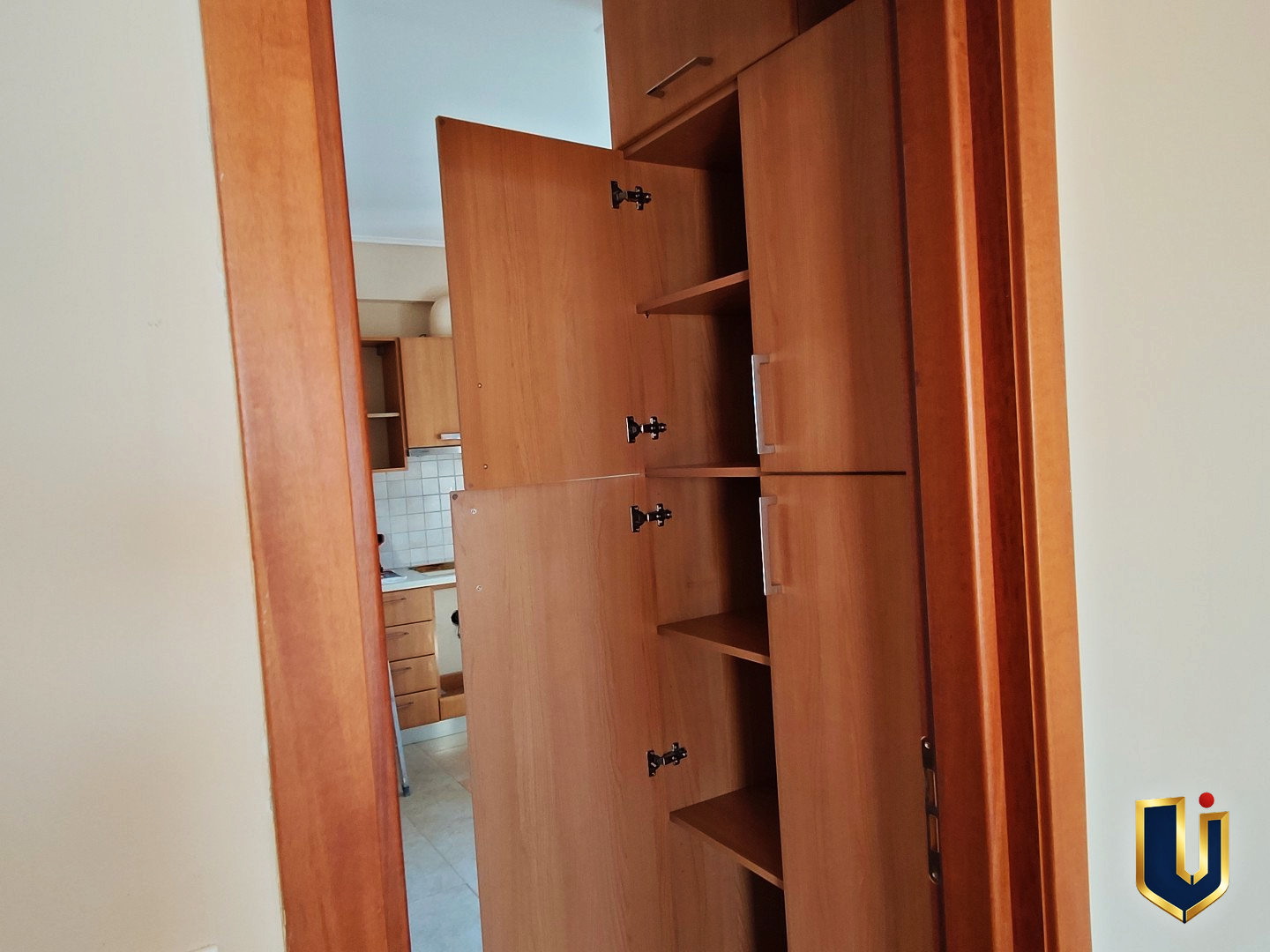 Tall wooden kitchen cupboard with open doors and internal shelves in a Paiania apartment