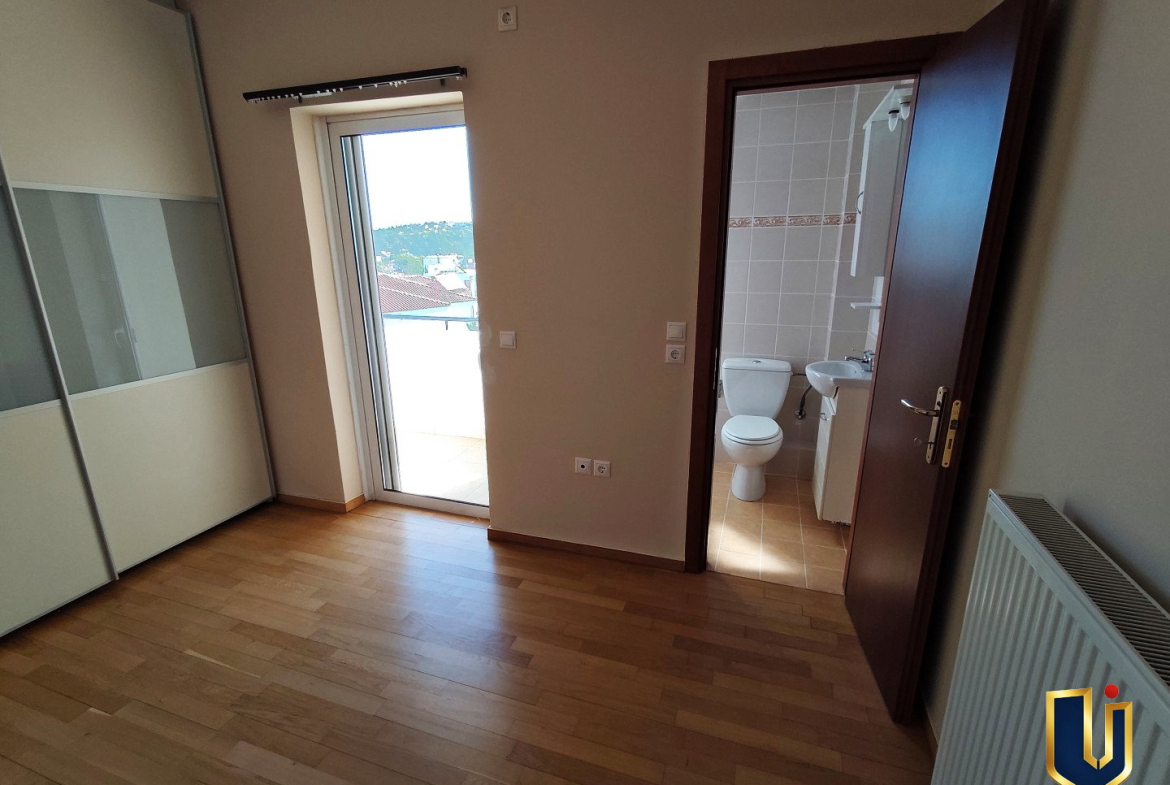 Main bedroom in a Paiania apartment with parquet flooring, fitted wardrobe, balcony access and an en-suite doorway