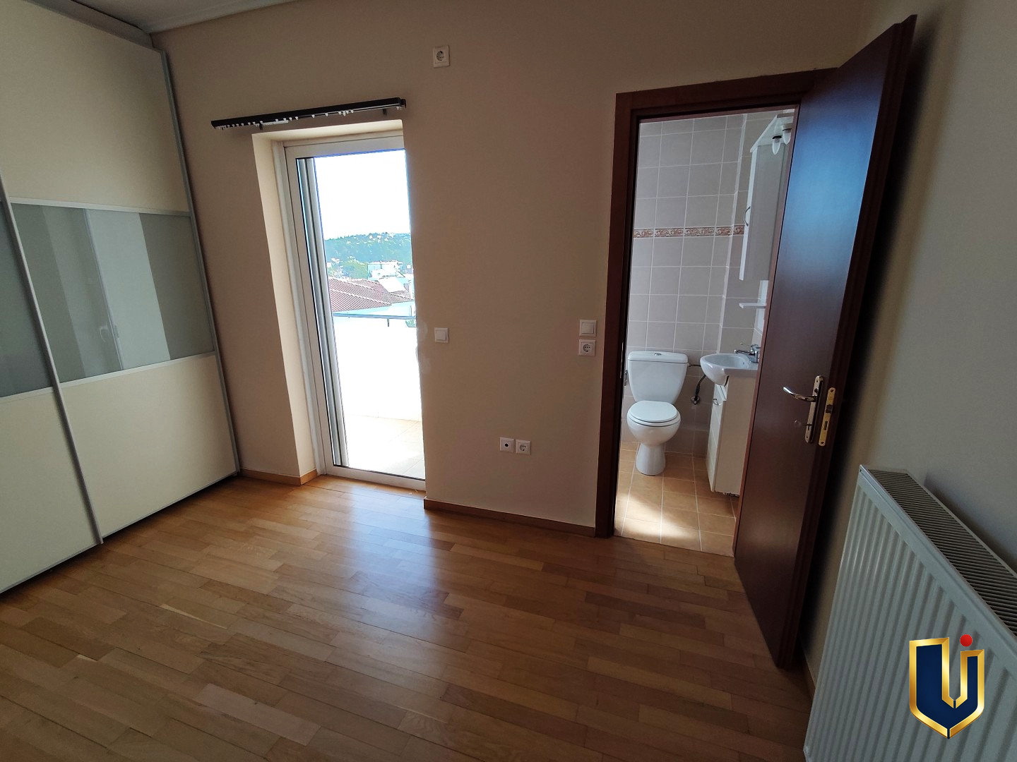 Main bedroom in a Paiania apartment with parquet flooring, fitted wardrobe, balcony access and an en-suite doorway