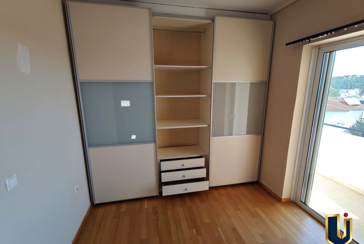 Main bedroom in Paiania with a partially open sliding-door wardrobe, shelves, drawers and balcony access