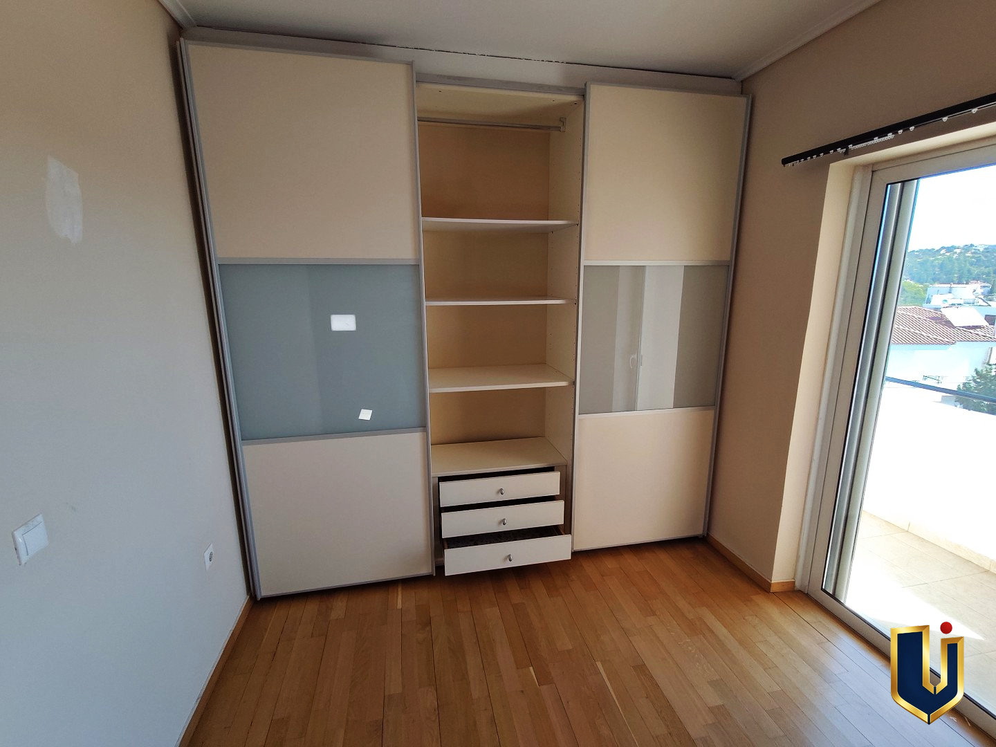 Main bedroom in Paiania with a partially open sliding-door wardrobe, shelves, drawers and balcony access
