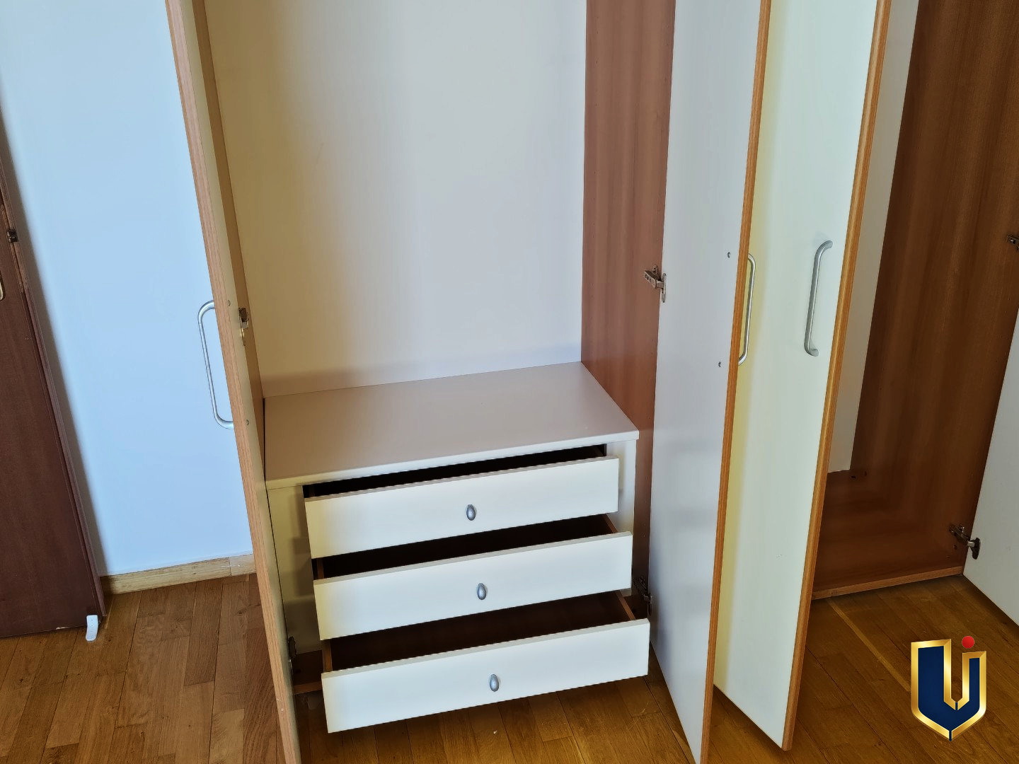Open fitted wardrobe showing hanging space and three drawers in the second bedroom of a Paiania apartment