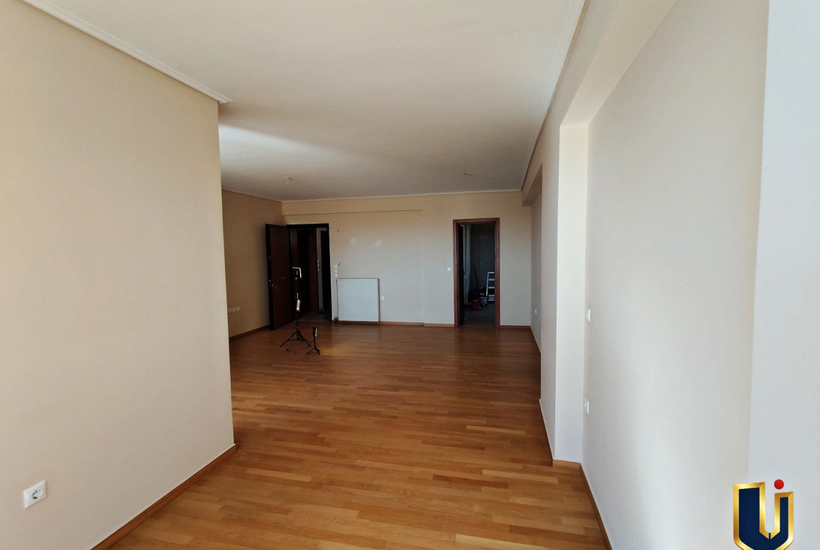 Living room with parquet flooring and white walls, looking towards the entrance and kitchen doorway in a Paiania apartment