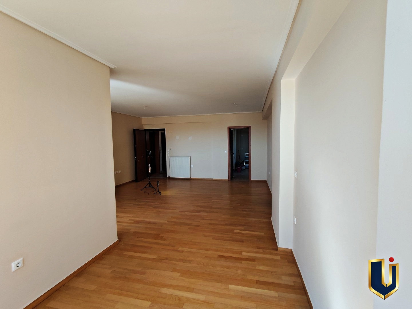 Living room with parquet flooring and white walls, looking towards the entrance and kitchen doorway in a Paiania apartment