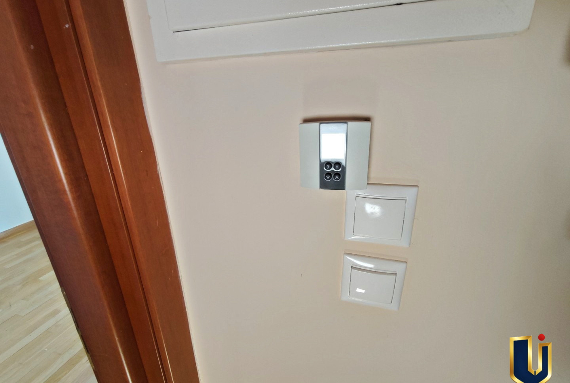 Wall-mounted digital thermostat and light switches beneath the electrical panel in a Paiania apartment