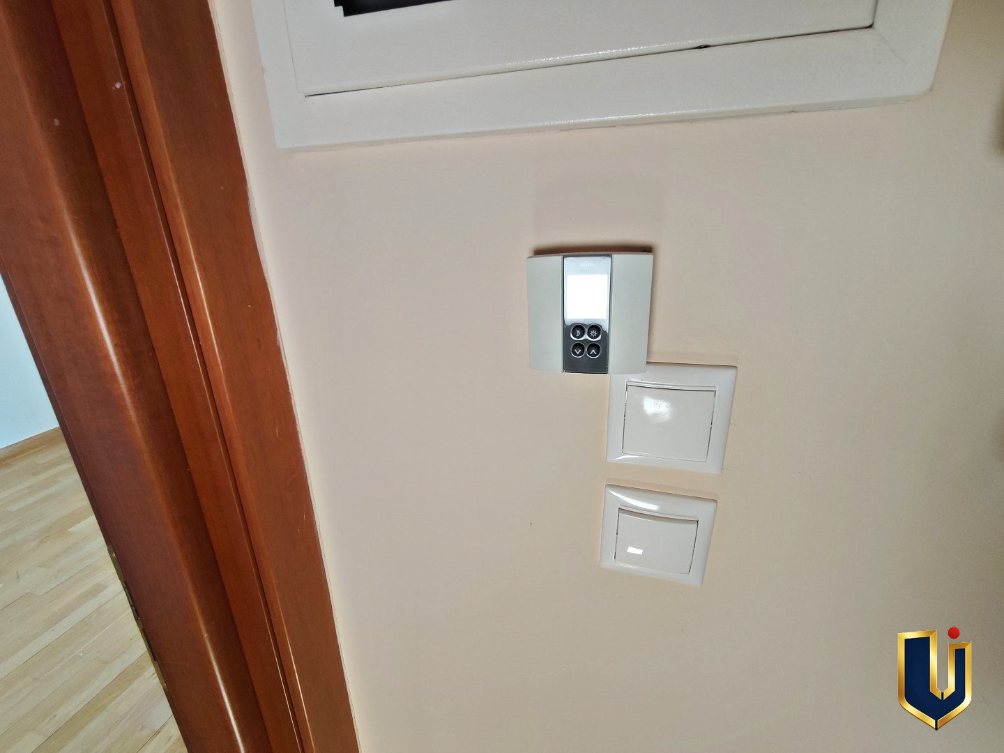 Wall-mounted digital thermostat and light switches beneath the electrical panel in a Paiania apartment