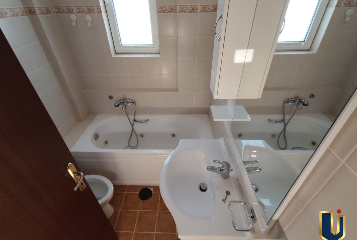 Main bathroom with a bathtub, washbasin, large mirror and window in a Paiania apartment