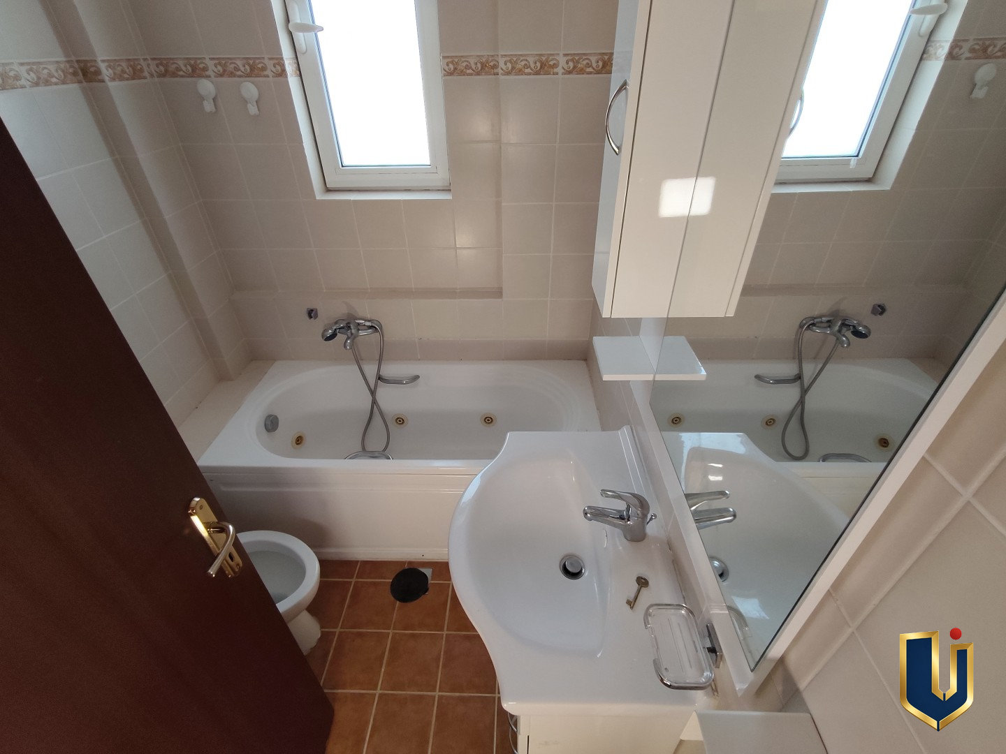 Main bathroom with a bathtub, washbasin, large mirror and window in a Paiania apartment