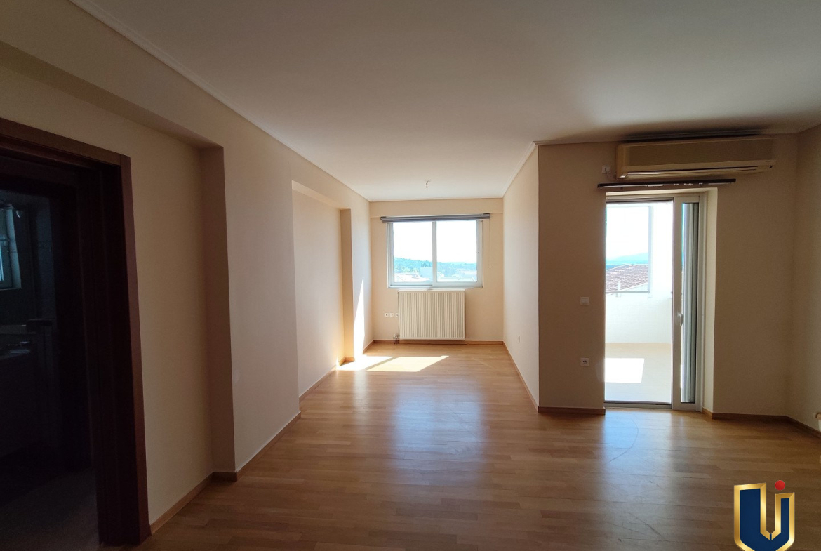 Spacious living room with parquet flooring, a window and glazed balcony door in a Paiania apartment