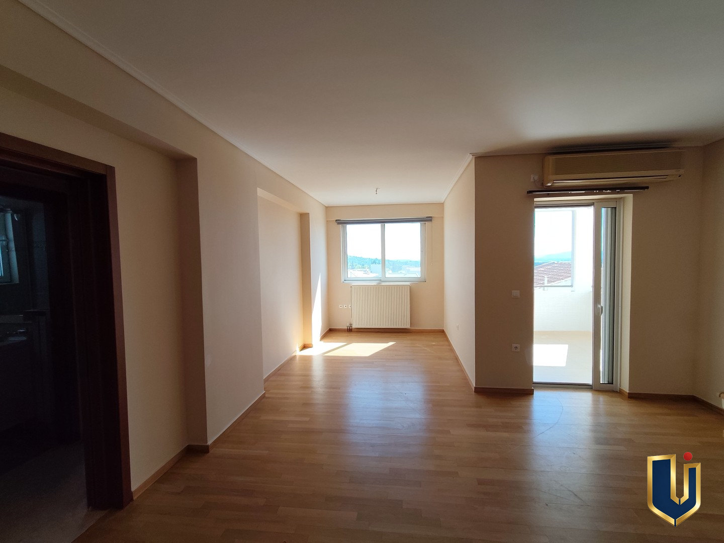 Spacious living room with parquet flooring, a window and glazed balcony door in a Paiania apartment