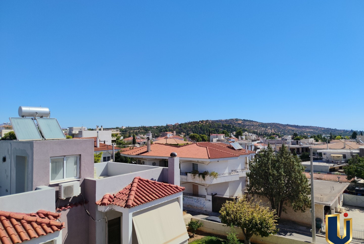 View from a Paiania apartment bedroom over neighbouring homes, tiled rooftops and trees towards a distant hill