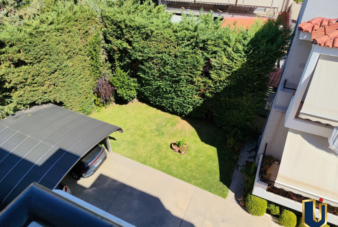 Downward view from the second bedroom of a Paiania apartment over a garden with lawn, trees and hedges