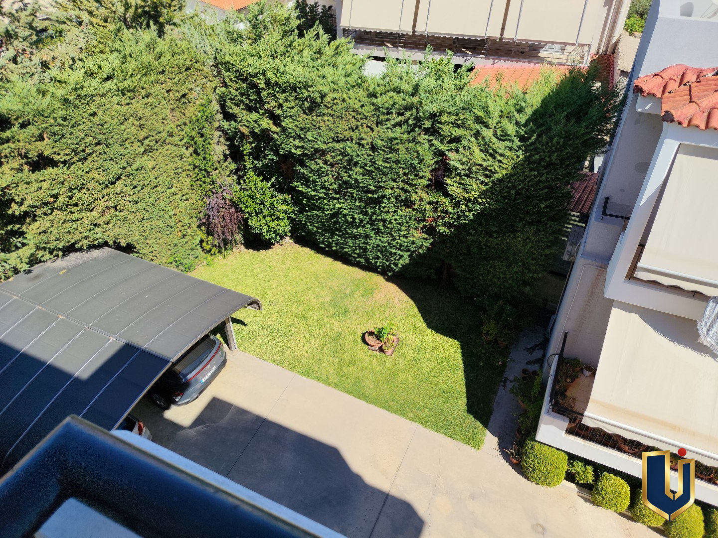 Downward view from the second bedroom of a Paiania apartment over a garden with lawn, trees and hedges