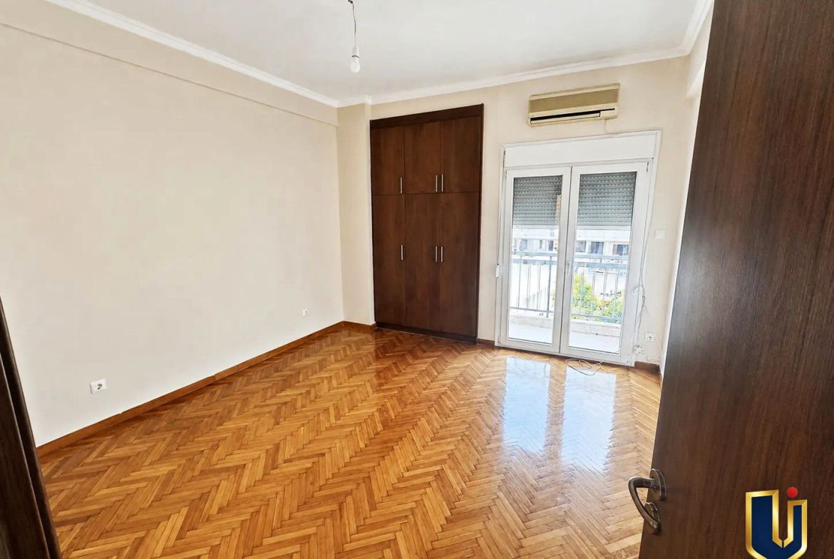 Second bedroom with wooden flooring and a balcony door in a renovated penthouse in Kato Patissia, Athens.