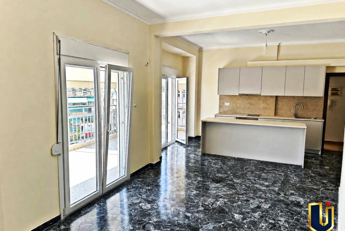 Renovated kitchen with a dark countertop and balcony doors in a penthouse in Kato Patissia, Athens.