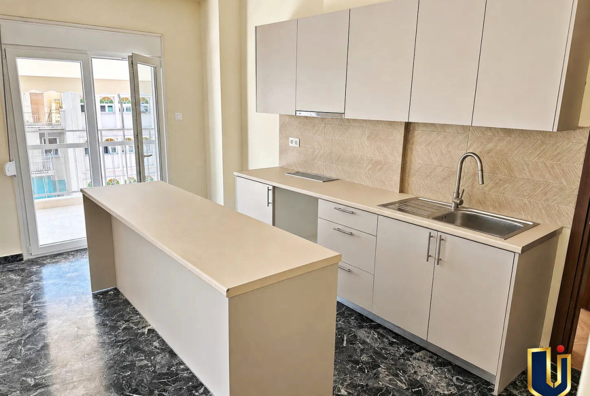 Modern kitchen with white cabinets and a central island in a renovated penthouse in Kato Patissia, Athens.