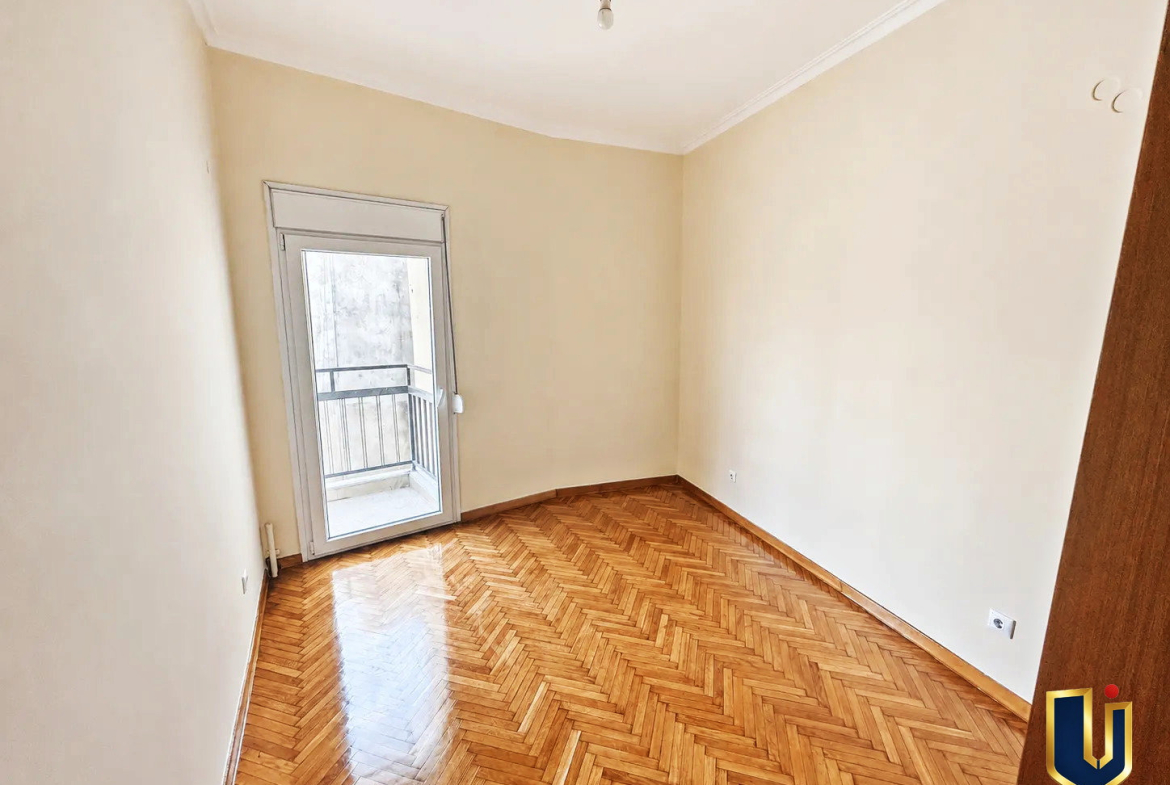 Bright, unfurnished children’s bedroom with wooden flooring and a large window in a renovated penthouse in Kato Patissia, Athens.