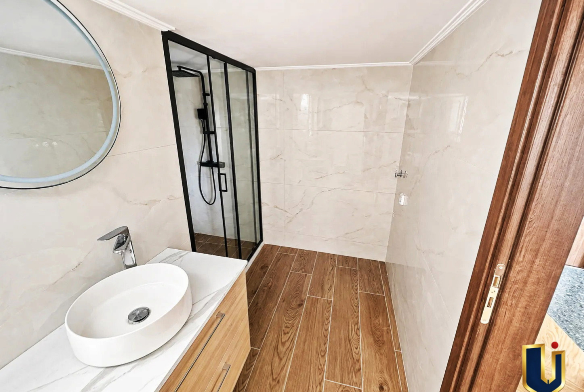 Compact bathroom with a toilet, glass shower enclosure, and light tiled walls in a renovated penthouse in Kato Patissia, Athens.
