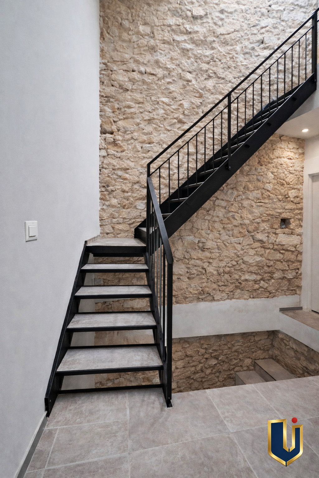 Interior staircase with a dark railing beside a stone-textured wall.