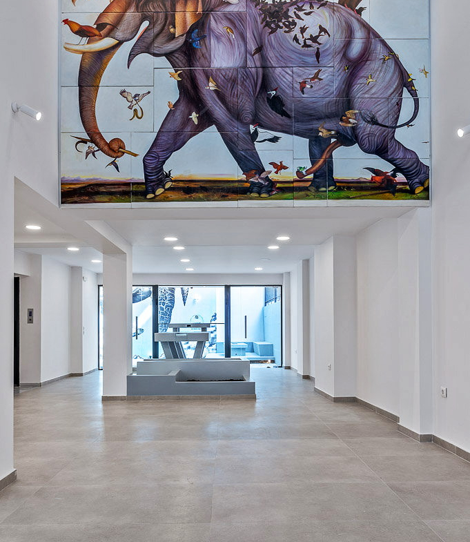 Interior lobby of an Athens building featuring a large elephant mural and a bright glass entrance